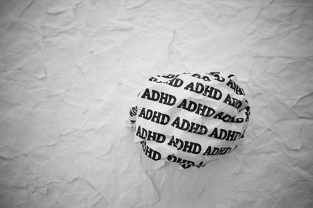 Crumpled paper ball with words ADHD on torn white paper pieces background.の写真素材