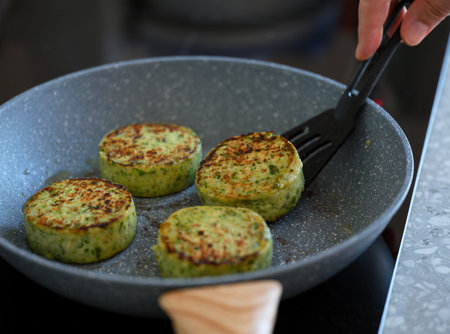 A woman flipping vegetable patties in a frying pan with a spatulaの写真素材