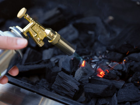 Person using a blowtorch to light charcoal in a grill