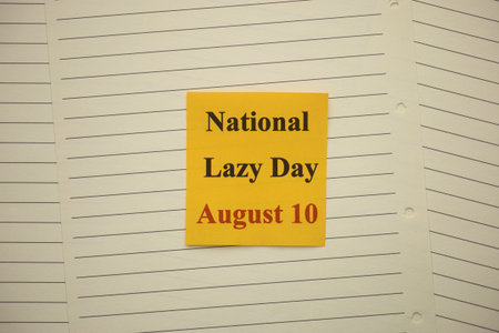 Yellow paper note with words National Lazy Day August 10 lying on lined notebook pages
