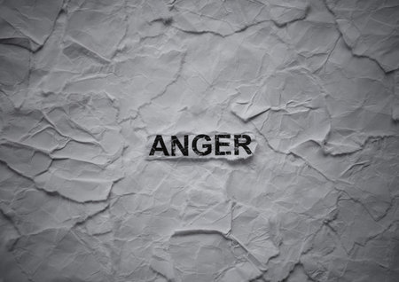 Crumpled piece of paper with word Anger on torn crumpled white paper pieces background.の写真素材