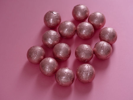 Group of chocolate spheres wrapped in pink foil scattered on a pink background.