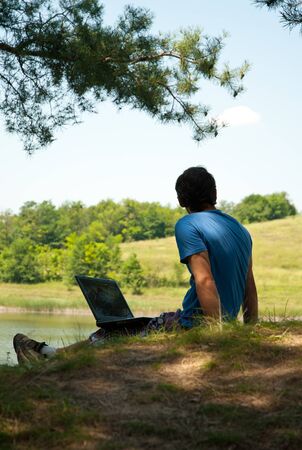 Man with laptop on river bankの写真素材