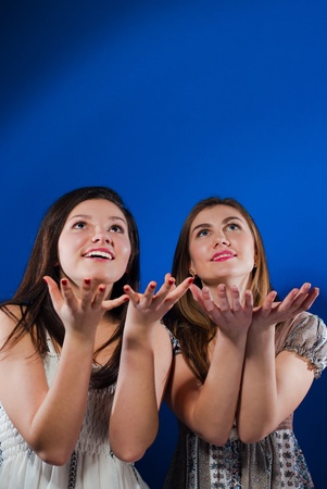 Two happy smiling teenage girls ready to catch from up empty space blue screenの写真素材