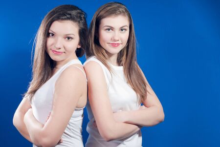Two young happy women standing back to back over bluescreenの写真素材