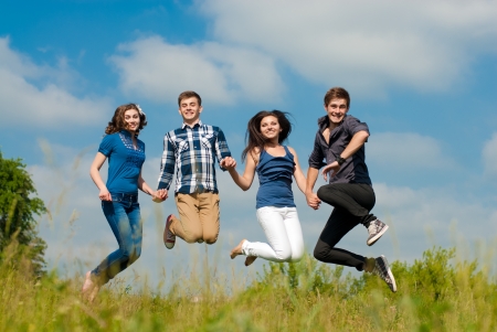 Happy four teenage friends jumping against blue skyの写真素材