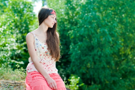 Young pretty teenage girl in hippie style cloth sitting against green leaves backgroundの写真素材