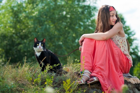 Young happy smiling teenage girl sitting on rock and holding black cat on leadの写真素材