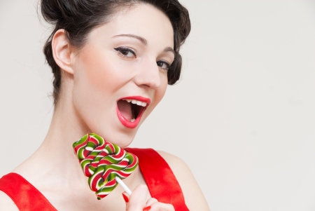 Funny beautiful happy pin up girl in red dress eating lollipopの写真素材