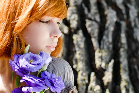 Young beautiful red hair teenage woman model holding purple chinese rose against tree rindの写真素材