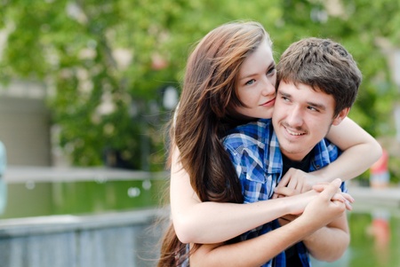 Young happy smiling teen couple man and woman embracing on green park backgroundの写真素材