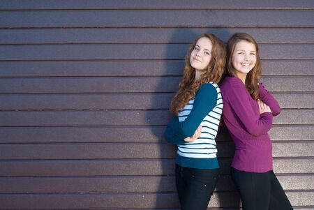 Two best teenage girlfriends standing back to back against grey violet backgroundの写真素材