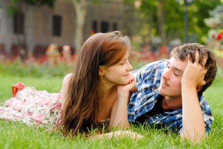 Happy young teenage couple man and woman in love lying on green grass in city parkの写真素材
