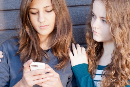 Teenage girl comforting her friend reading sad messageの写真素材