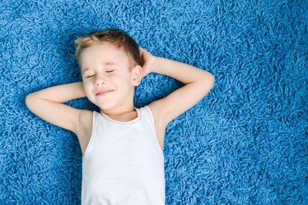 Happy boy smiling kid on blue carpet in living room at homeの写真素材
