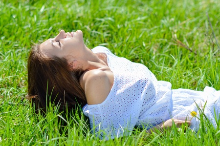 Happy young woman in short white summer dress lying on green grassの写真素材
