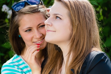 Two happy teen girl friends whispering secret on bright summer day outdoorsの写真素材