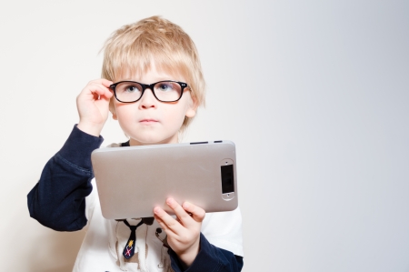 Little boy in eye glasses reading or playing on tablet pc in studio