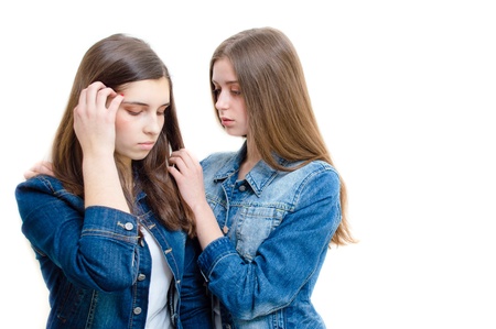 Two beautiful young women in jeans jackets comforting one another on white backgroundの写真素材