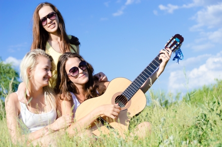 Three happy teen girls singing and playing guitar against blue sky on bright summer dayの写真素材