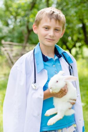 young happy boy in doctor cloth embracing little rabbit outdoors on summer dayの写真素材