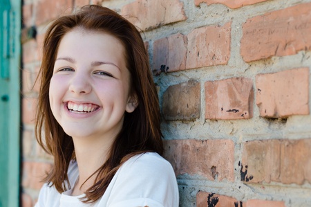 Young happy teenage girl standing at red brick wall background copyspaceの写真素材