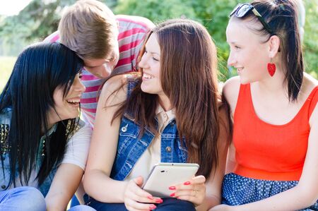 Four happy teen friends laughing on picture of themselves on tabletの写真素材