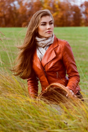 Beautiful young woman sitting in high grass on cold windy autumn dayの写真素材