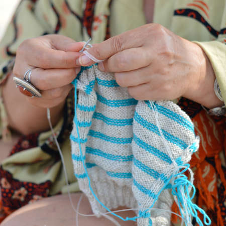 Happy mature woman sitting on beach and knitting hands closeup