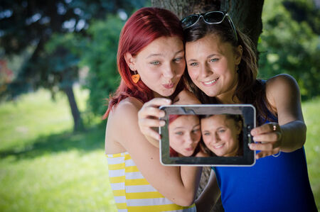 Two young women teenage girls students sitting in park with tablet pc