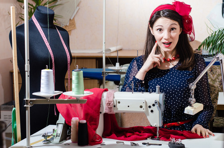 portrait of funny beautiful young pinup woman with sewing machine looking at camera surprisedの写真素材