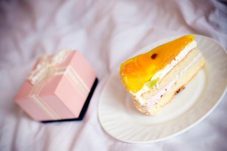 closeup on one great pink box of present or gift and delicious slice of cake on a plate on the white backgroundの写真素材