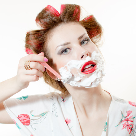 Beautiful young pinup woman shaving face looking in camera isolated on white backgroundの写真素材
