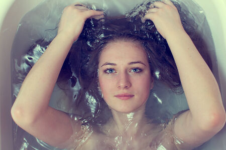 closeup portrait of beautiful blond young woman washing her hair in water & looking at camera in waterの写真素材