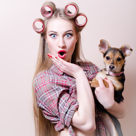 closeup picture of beautiful blond young pinup woman blue eyes girl having fun playing with cute small dog looking at camera surprised and happy smiling portraitの写真素材