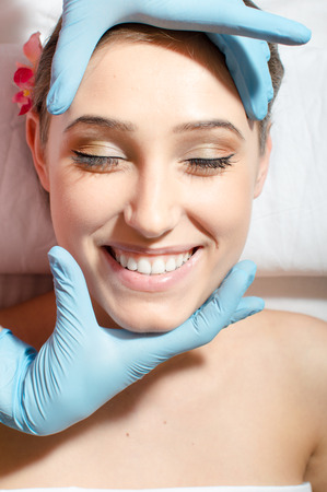 enjoyable face massage: close up of beautiful young woman sexy attractive girl with great dental care having fun on spa procedures happy smiling relaxing eyes closed & laying on white bed portraitの写真素材