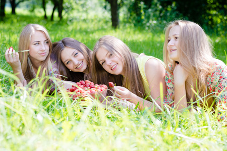 4 beautiful young women girl friends having fun eating strawberries on summer green outdoors background pictureの写真素材