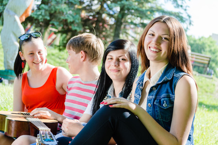 portrait of friends young women and handsome boy sitting together in forest having fun