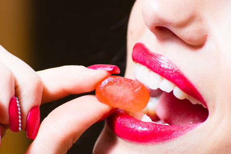 closeup image on fingers with red color nails holding candy at seductive charming beautiful red lips...