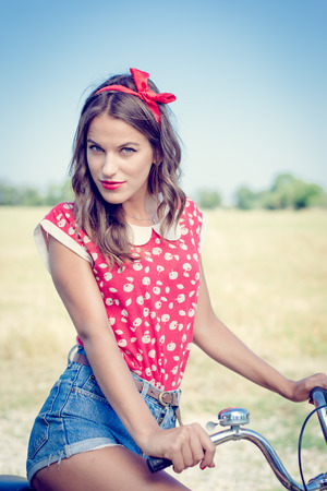 Young pinup woman cycling with flowers in basket under bright blue summer skyの写真素材