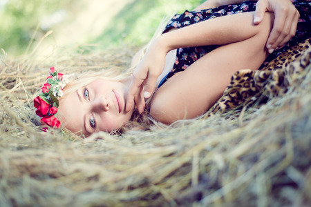 closeup portrait of fashion happy pretty girl with blue eyes having fun laying on hay smiling & looking at camera on green summer outdoors copy space backgroundの写真素材