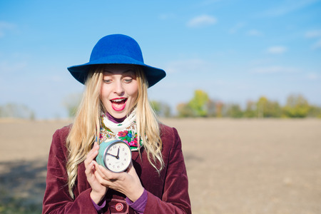 portrait of elegant beautiful blond young woman having fun holding retro alarm clock on sunny autumn outdoors copy space backgroundの写真素材