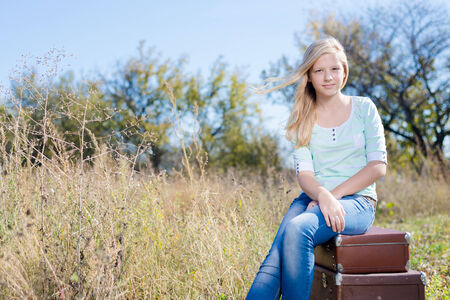 Portrait of pretty teenage girl sitting on three retro suitcases outdoors on autumn field copy space backgroundの写真素材