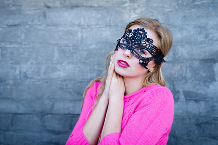 Young blond sensual woman in black lace mask over gray brick wall copy space backgroundの写真素材