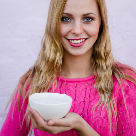 Happy young blond woman drinking hot tea or coffee and looking joyful over pin brick wall copy space backgroundの写真素材