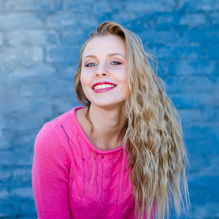 beautiful blond young lady in pink sweater at blue concrete wall copy space background
