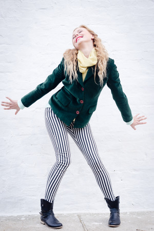 Happy young blond hipster woman wearing stripped trousers funny posing over white brick wall copy space backgroundの写真素材