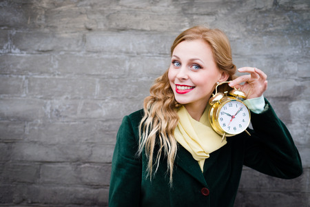 Pretty hipster teenage girl with golden alarm clock smiling at gray wall background copy space imageの写真素材