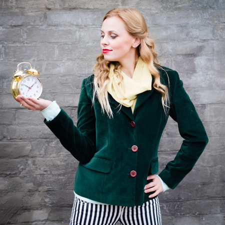 Pretty hipster teenage girl with golden alarm clock smiling at gray wall background copy space imageの写真素材