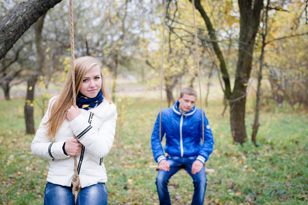 Happy teen couple outdoors on cold autumn day sitting on swingsの写真素材